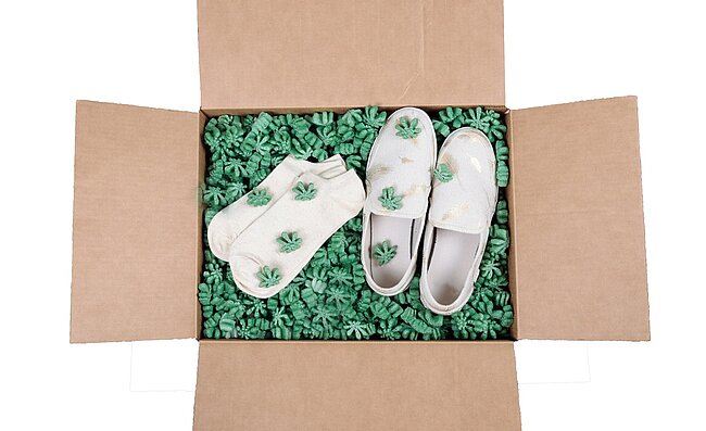 Ein Karton mit einem Paar Schuhe und Socken und grünem Loose Fill