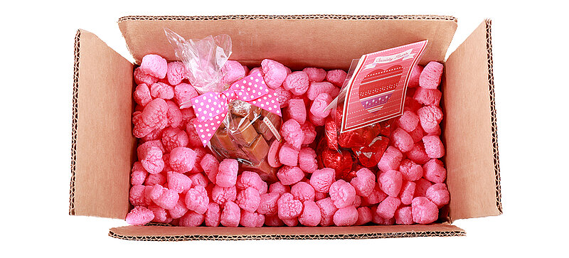A cardboard box containing confectionery and pink, heart-shaped packaging chips