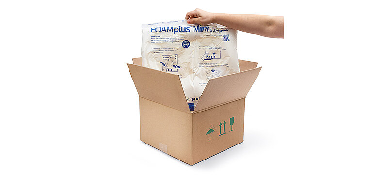An arm holds up a FOAMplus Mini foam cushion that was previously placed in a cardboard box