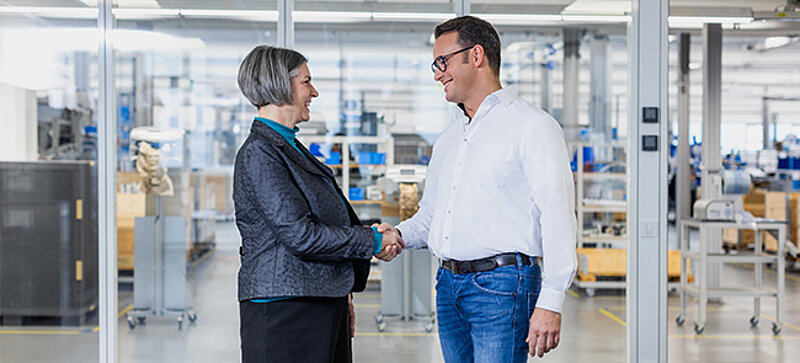 
		  Business handshake between two people in a warehouse setting.