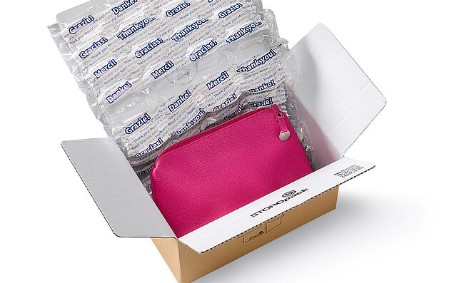 A cardboard box containing a pink bag and air cushions with a printed design