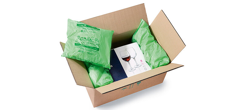 A box with a box of wine glasses padded with plastic bags with packing chips